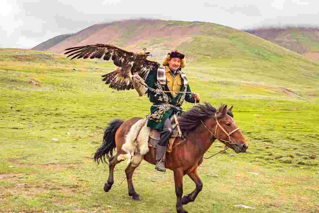 Eagle hunter in traditional dress riding a horse in Mongolia