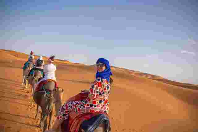A traveller smiling as she rides a camel through the Sahara Desert in Morocco