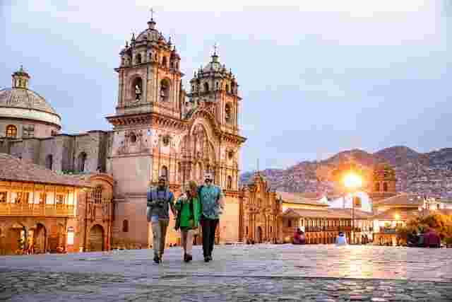 A group of people walking in front of the cathedral in Cusco at twilight. 