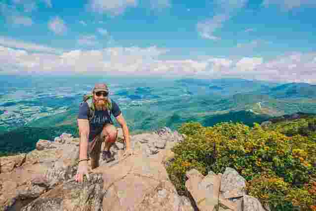 A hiker crouching on a ledge overlooking the Appalachian Mountains