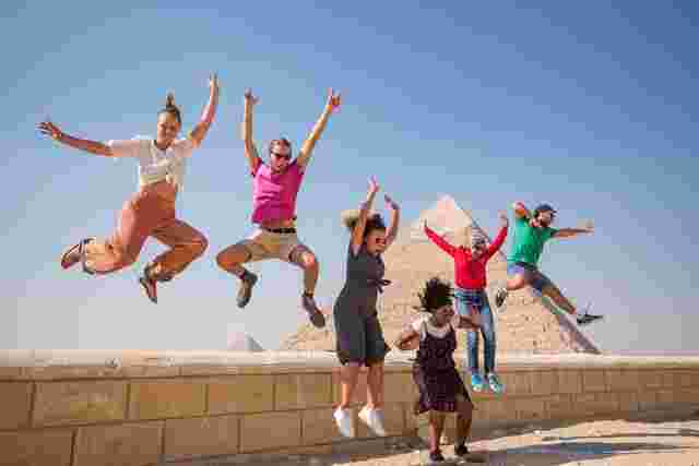 A group of people jump in the air in front of the Pyramids