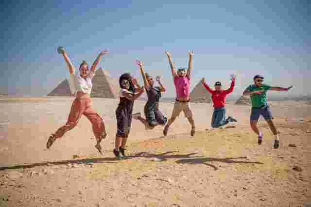 Intrepid travellers and leader jump for joy in front of the Pyramids at Giza