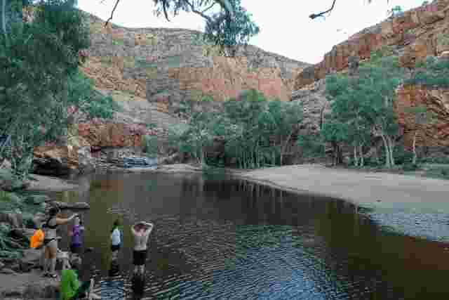 A group of people gathered at the edge of a natural swimming hole along the Larapinta Trail