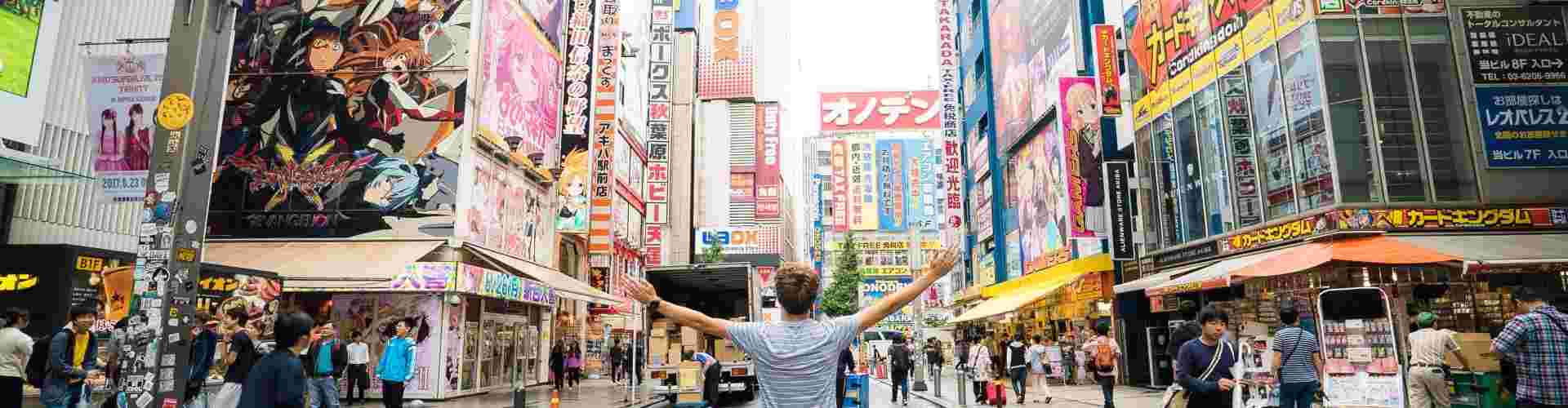 Man standing in the middle of a busy street in Tokyo's anime district with his arms out wide.
