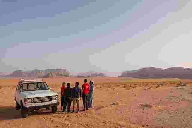 A group of travellers and a guide standing by a jeep in Wadi Rum, Jordan