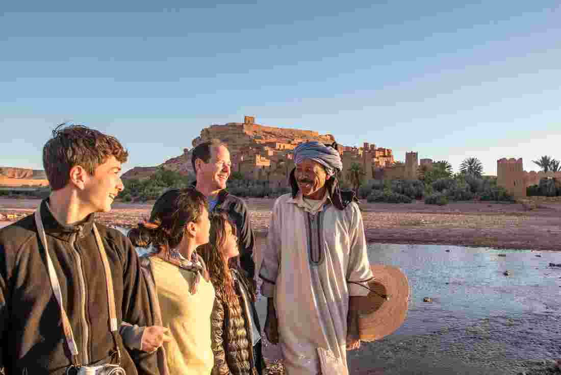 A family of travelers gathers with a local at Ait Benhaddou in Morocco