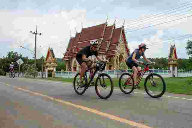Two cyclists riding past a temple in Thailand