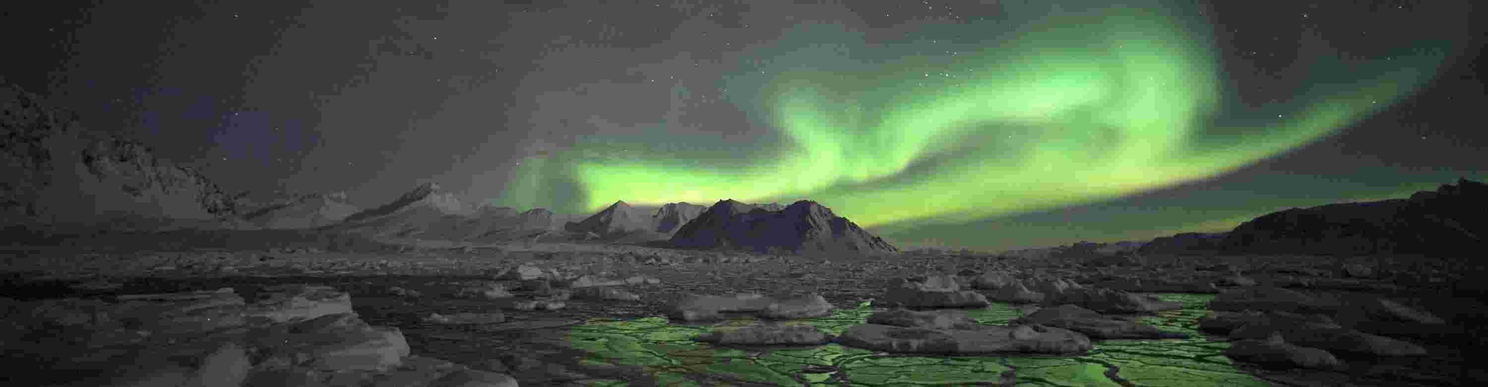 A swirling green lightshow of the Aurora Borealis above a snowy Alaskan landscape
