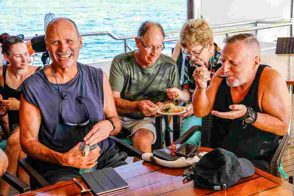 A group of 5 travellers sharing a meal on the deck of their adventure cruise in Thailand