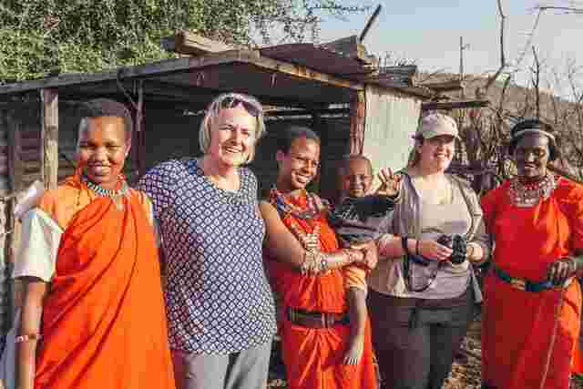 A group of travelers standing with local Maasai women in the campsite at Loita Hills