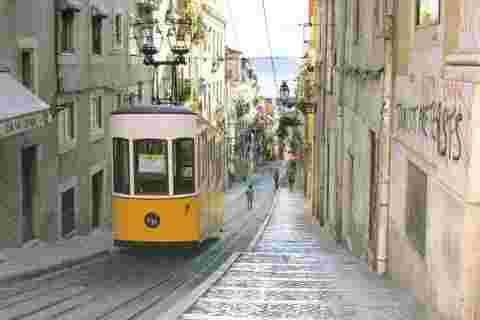 A traditional tram travelling up a narrow street in Lisbon
