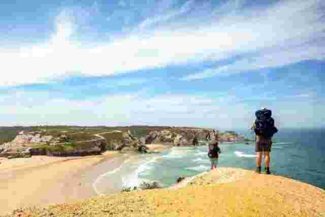 A group of hikers walking along the sandy coast of Rota Vicentina on a sunny day. 