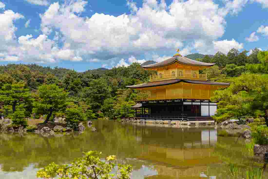 Kinkaku-ji Temple Golden Pavilion at the edge of a curated pond on a sunny day with clouds above