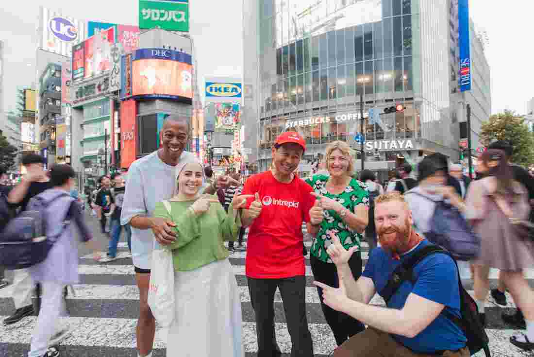 Group of Intrepid travellers point to the leader amidst a crowd at Shibuya crossing