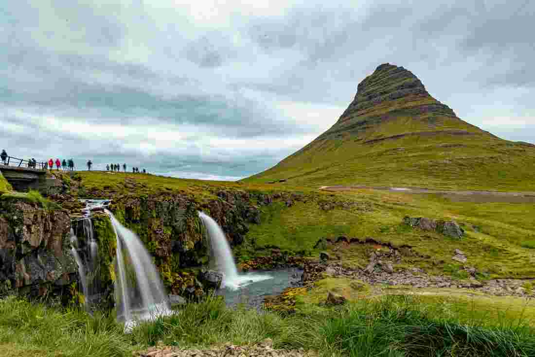 Group of travellers stand above Kirkjufelsfoss waterfall on the Snæfellsnes Penninsula