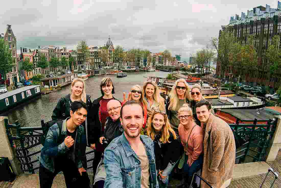 Group of travellers pose for a selfie smiling on a canal bridge in Amsterdam
