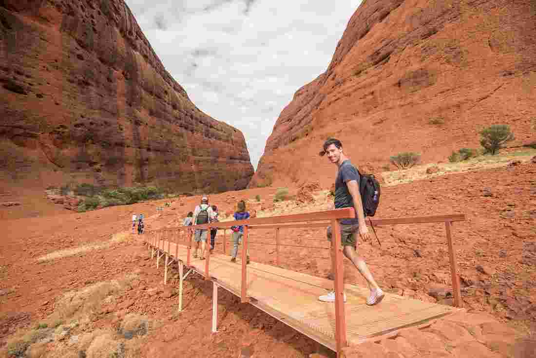 Male traveller and group crossing bridge hiking through Uluru