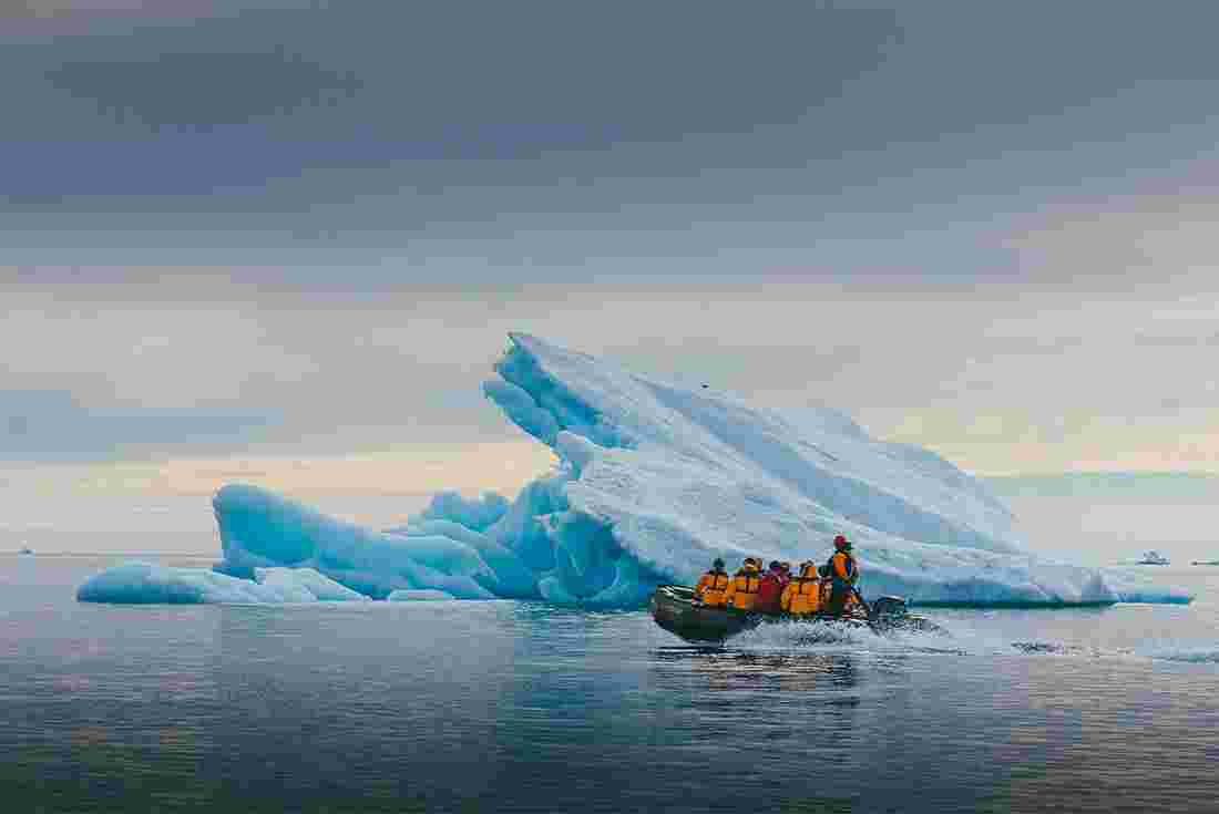 Group of travellers cruise past an upturned iceberg in a zodiac