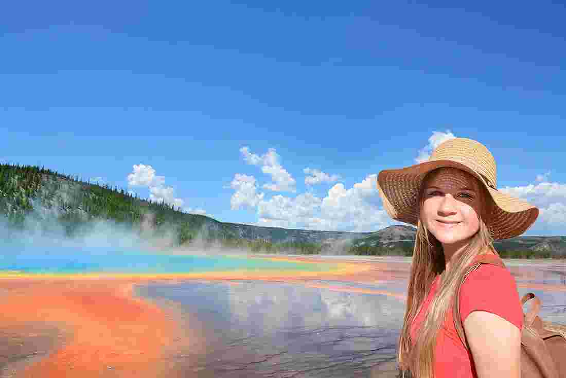 Young girl smiling in front of colourful Prsimatic Spring in Yellowstone NP, Wyoming, USA