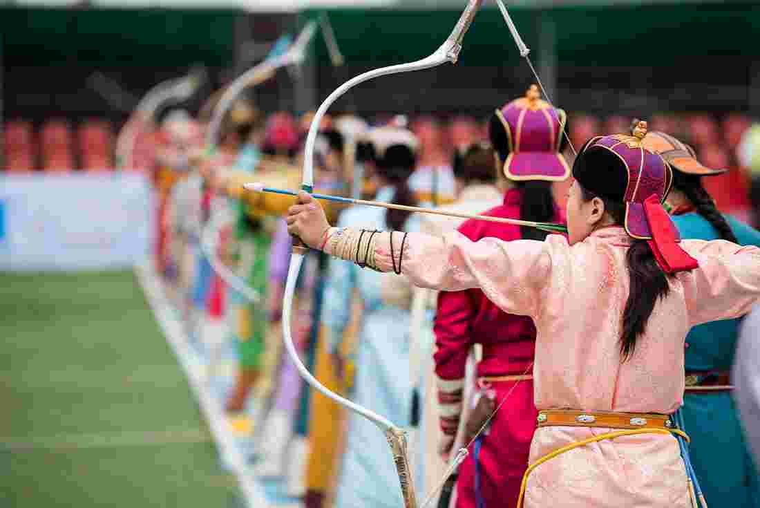 Naadam festival women's archery, women in traditional Mongolian dress shooting arrows with Mongol bow and arrow
