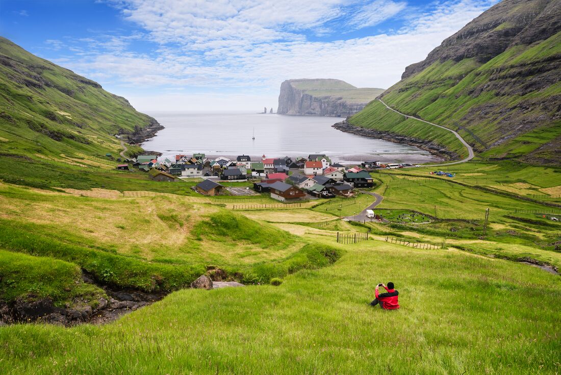 Intrepid traveller perched on the hills above Gjogv viewing to Risin og Kellingen in theh Faroe Islands