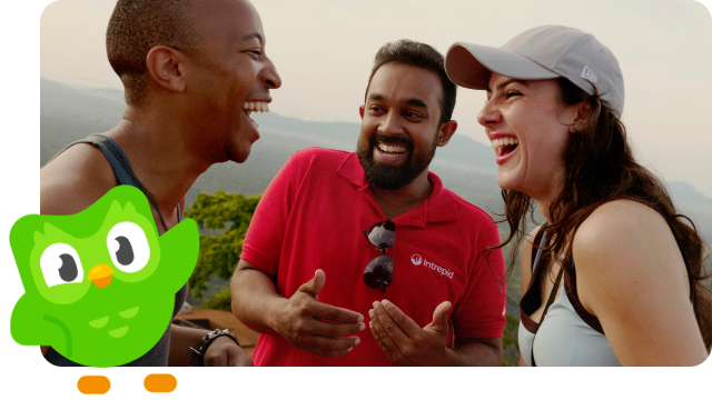 Two travellers smile and laugh with their leader, joined by the Duolingo owl.