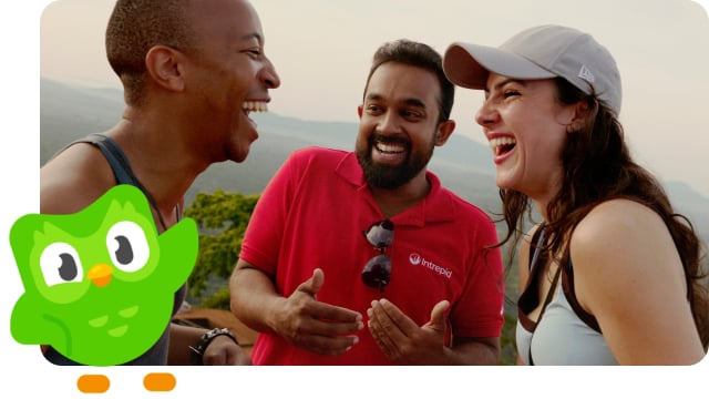 Two travellers smile and laugh with their leader, joined by the Duolingo owl.