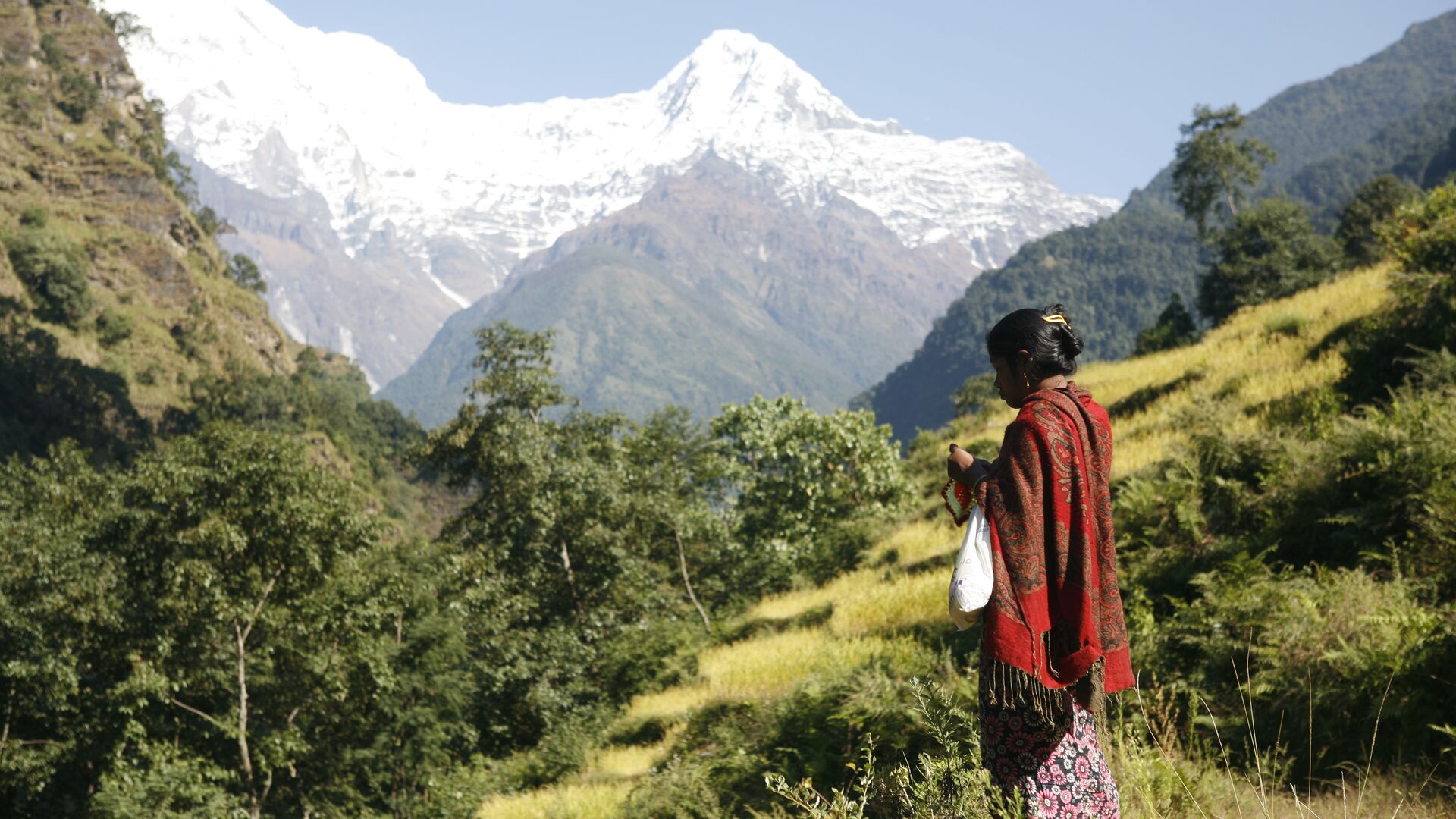 A woman stands with her back turned with a mountain range in the background.