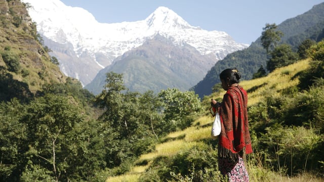 A woman stands with her back turned with a mountain range in the background.