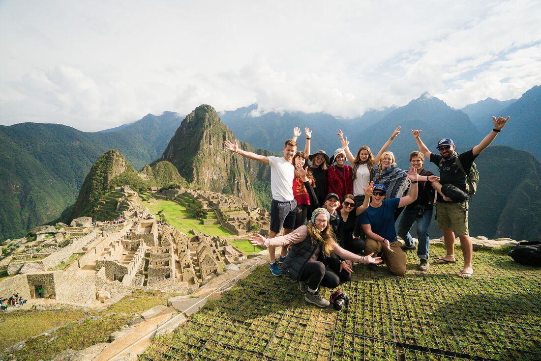 Group of excited travellers in activewear pose at the Machu Picchu lookout in Peru