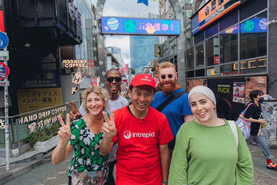 Intrepid Leader with traveller group posing with peace signs at the entrance of Takeshita Street, Harajuku, Tokyo, Japan