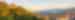 A church sits on a hill filled with trees in Romania and the hill descends into the valley village.