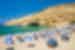 Travellers on the beach with blue and white parasols Matala beach with cliff in background, Crete, Greece