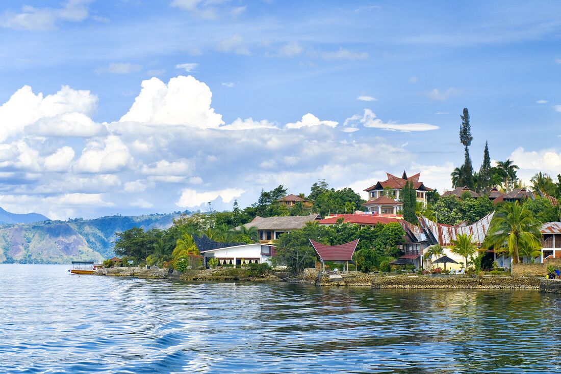 Samosir Island houses with traditional Batak houses amidst trees and the lake stretching out from shore with mountains behind