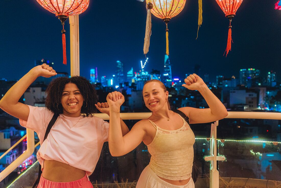 Travellers having drinks at a rooftop bar with night cityscape lights behind them in Ho Chi Minh City, Vietnam