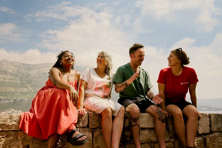 Travellers sitting on a stone wall against a panoramic view in Korcula, Croatia