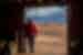 Traveller in red looks out from desert home at Agafay Desert with Atlas Mountains in distance