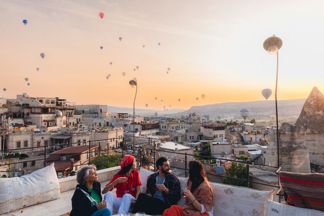 Travellers enjoying the view of hot air balloons at sunset while drinking tea, Cappadocia, Turkey
