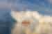 Small orange and white ship Disko Bay ferry overshadowed by huge iceberg in Disko Bay Greenland