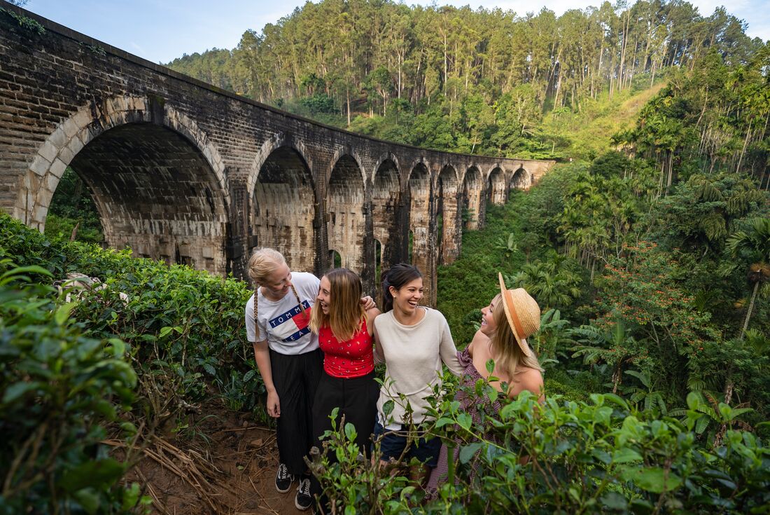 Four young Intrepid travellers laugh together with the Nine Arches bridge behind them in Sri Lanka