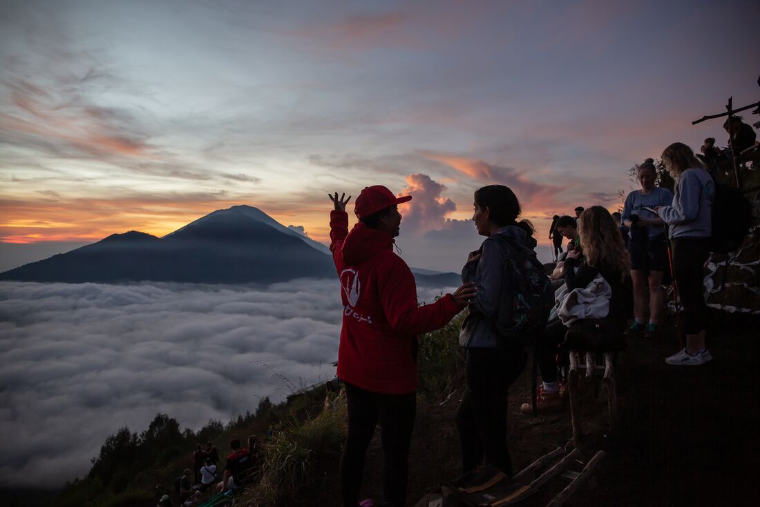 Leader with travellers enjoying the view of a glowing sunrise during the Mount Batur hike, Bali, Indonesia