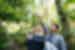 A local leader stnads in the middle of the forest, he is pointing up at the trees and a group of three people are staring up