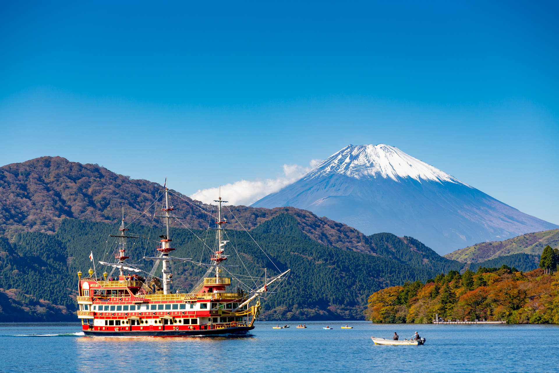 A bright red pirate ship sails on Lake Ashi with Mount Fujji behind