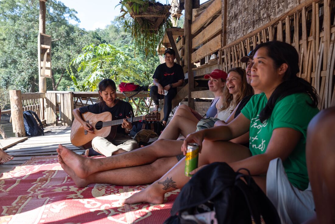 Travellers laughing with local playing the guitar during a hilltribe village homestay in Mae Taeng District, Chang Mai, Thailand