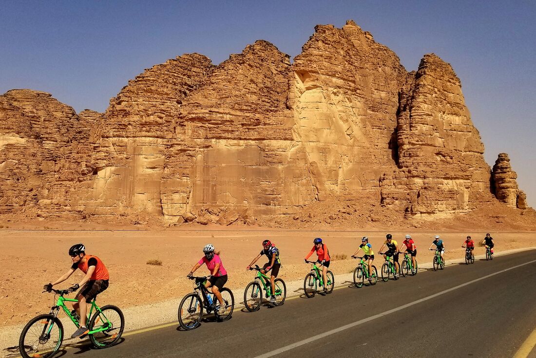 Travellers cycling in single file on road passing sandstone mountain in Wadi Rum desert, Jordan