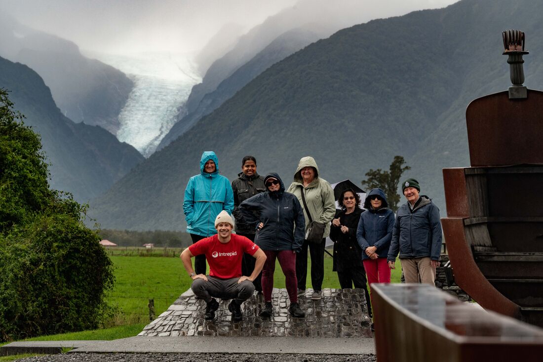 Intrepid Leader takes a photo with traveller group in front of Fox Glacier, New Zealand