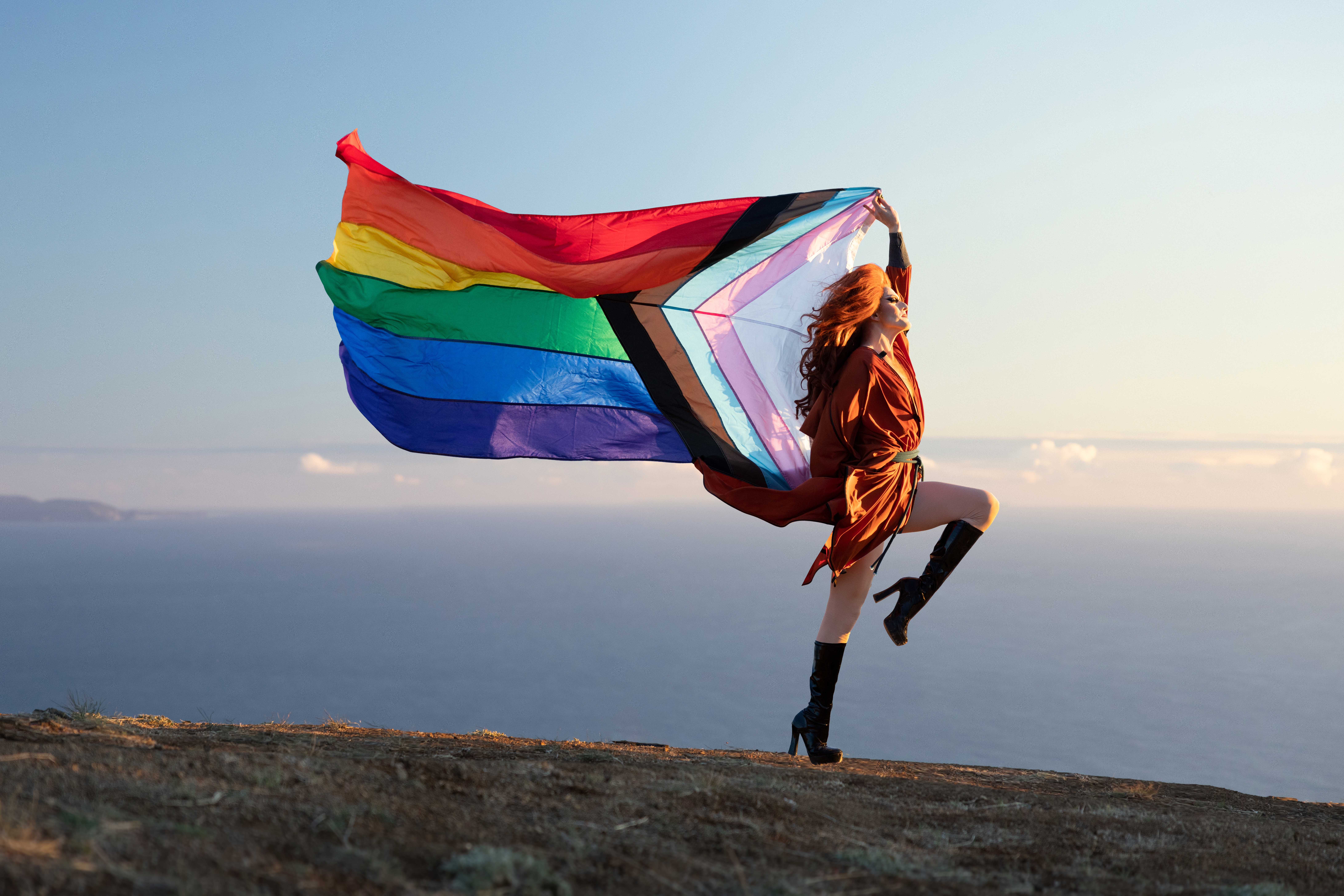 Drag queen Pattie Gonia poses outside with a colourful Pride flag
