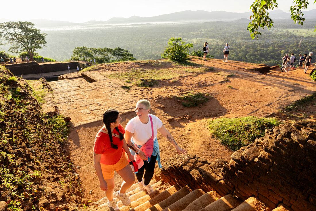 Travellers walking up stairs at Lion Rock Fortress with grand landscape views behind them, Dambulla, Sri Lanka