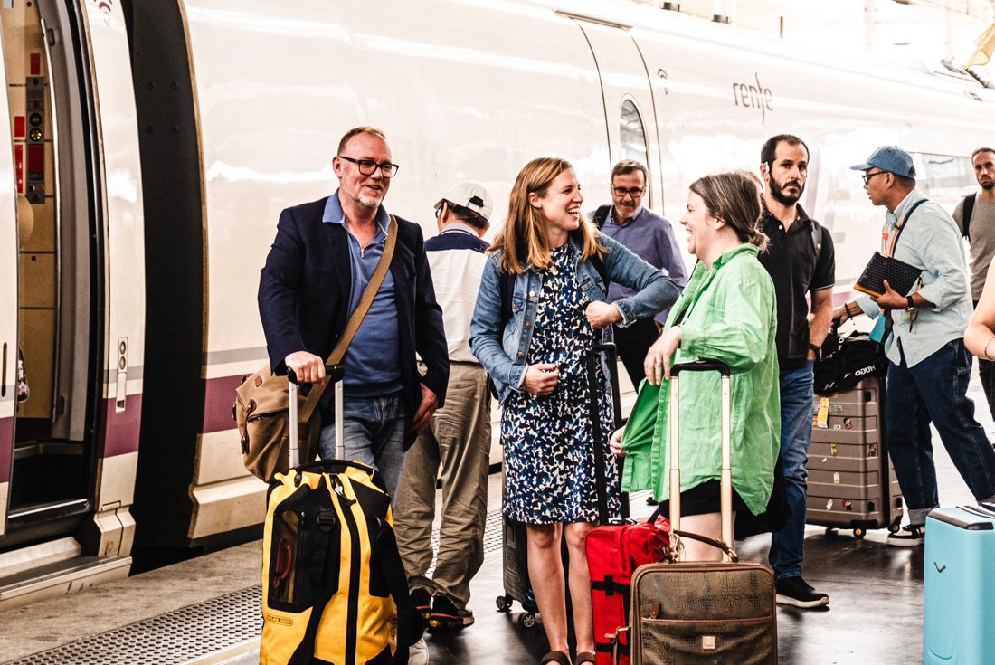 Travellers laugh together at Madrid station with luggage getting off a train