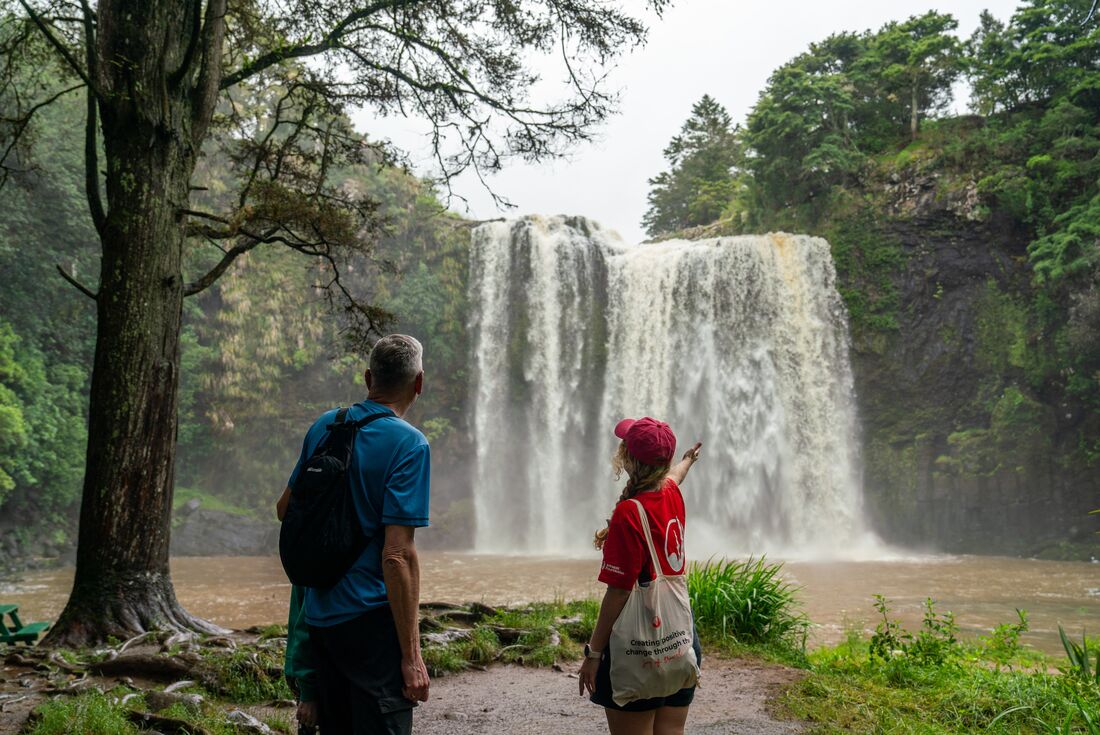 Leader with traveller standing in front of crashing waters of Whangarei Falls, New Zealand